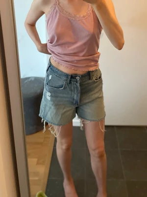 Blå jeansshorts med fransig kant från HM - Säljer ett par blå jeansshorts från HM i storlek 36 med normal midja och fransig kant nertill. Shortsen har slitna detaljer framtill. 25 kr!