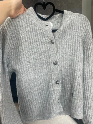 Grå ribbstickad kofta med knappar - Mysig grå kofta i ribbstickat material med rund halsringning och fyra stora knappar framtill. Finns inte i butik längre 