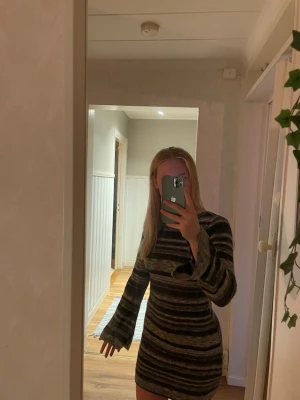 Randig stickad klänning med öppen rygg - Kort, stickad klänning! Klänningen har långa trumpetärmar och en snygg öppen rygg. Perfekt för dig som vill ha något både bekvämt och trendigt. Använd en gång!