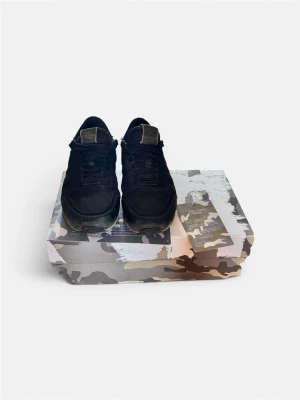 Svarta sneakers från Valentino - Snygga svarta sneakers från Valentino med detaljer i mocka och mesh. Skorna har nitar på hälen och en kontrasterande brun sula. Perfekta för dig som vill ha en stilren men edgy look.