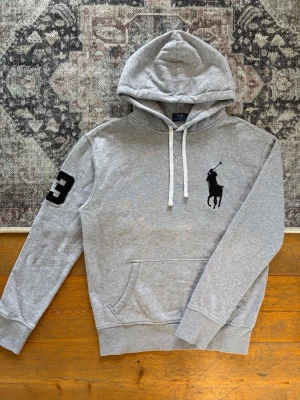 Ljusgrå Polo Ralph Lauren Hoodie Big Pony - Hej! 👋 Säljer en riktigt eftertraktad ljusgrå Polo Ralph Lauren Big Pony hoodie i storlek S med svart stram broderad logga samt "3"-applikation på ärmen. 🐎🔥 Tröjan är i fint skick överlag med alla tvättlappar kvar. Det finns en ytterst svag, nästan helt osynlig blekning på framsidan (syns knappt ens om man letar, se sista bilden). Perfekt tillfälle att nypa ett grymt och eftertraktat lyxplagg till ett nedsatt pris! Fraktar snabbt! 🚛📦💬 