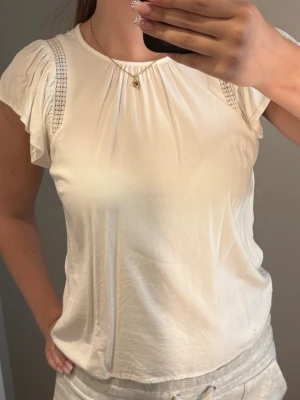 Vit blus med spetsdetaljer - Söt vit blus från Vero Moda med korta ärmar och fina spetsdetaljer längs axlarna och baktill. Luftigt och mjukt material, perfekt till sommaren💕