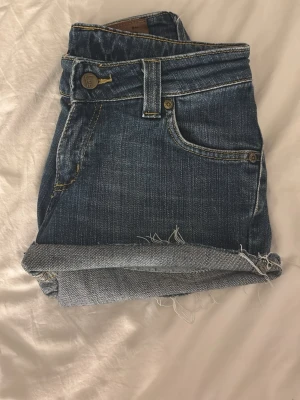 Blå jeansshorts från Lee - Snygga blå jeansshorts från Lee med råa kanter och klassisk femficksdesign. Shortsen har även en Lee-logga bak på linningen.💕