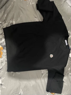 Svart sweatshirt från Moncler - Säljer en svart sweatshirt från Moncler med rund halsringning och Moncler-logga broderad på bröstet. Tröjan har en klassisk passform och ribbade muddar vid ärmslut och nederkant. Perfekt för dig som gillar stilrena och exklusiva plagg.
