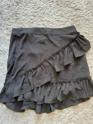 Svart volangkjol från ONLY - Säljer en svart kortkjol från ONLY med dubbla volangdetaljer och omlottkänsla. Kjolen har en mjuk struktur och är perfekt för dig som vill ha en trendig och bekväm look. Passar till både sneakers och boots. Skriv privat för fler bilder eller om du har några frågor💗
