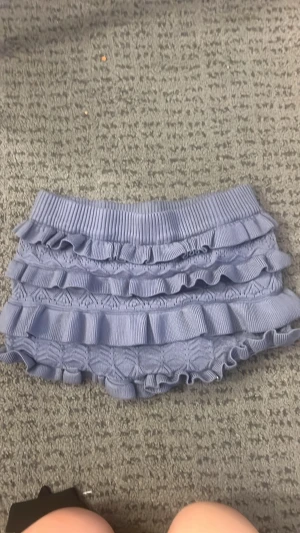Blå stickade shorts med volanger - Supersöta blå stickade shorts med flera lager volanger och ribbad midja. Shortsen har ett unikt mönster i stickningen och känns både mjuka och bekväma. Perfekta för dig som vill ha något gulligt och trendigt i garderoben.