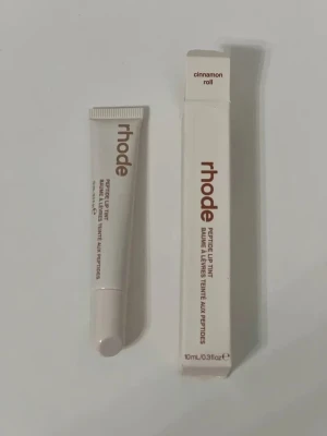 rhode Peptide Lip Tint Cinnamon Roll - Peptide Lip Tint från rhode i färgen Cinnamon Roll. Läppbalsamet kommer i en vit tub med brun text och matchande förpackning. Innehåller 10 ml och har en smidig applikator. Perfekt för dig som vill ha återfuktade läppar med en hint av färg.