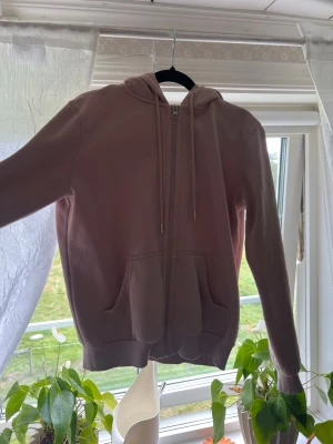 Rosa zip hoodie med huva - En enkel och snygg rosa hoodie med dragkedja framtill och två stora fickor. Hoodien har justerbar huva med snören och ribbade muddar vid ärmar och nederkant. Perfekt för en avslappnad och chill stil.
