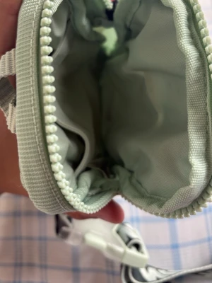 Ljusgrön Nike axelväska med logga - Axelväska i ljusgrönt från Nike med två broderade swoosh-loggor på framsidan. Väskan har justerbar axelrem med stor NIKE-text i vitt och svart. Materialet är slitstark textil med rutmönstrad struktur och dragkedja med repdetalj.