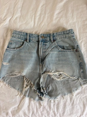 Ljusblåa högmidjade jeansshorts - Säljer ett par ljusblåa jeansshorts från Zara med hög midja och slitna detaljer. Shortsen har råa kanter, fem fickor och dragkedja med knapp. 