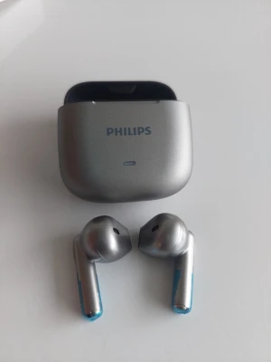 Philips trådlösa in-ear hörlurar - Snygga trådlösa in-ear hörlurar från Philips i metallic silver med matchande laddningsetui. Hörlurarna har en stilren design med blå detaljer på staven och är tillverkade i plast och metall. Perfekta för musik, poddar och samtal på språng.