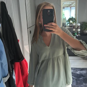 Ljusgrön v-ringad blus  - Säljer en ljusgrön blus med v-ringning, blusen har långa ärmar och har ett skönt och tunt material. Man kan knäppa på ärmarna så öppningen vid ärmarna stängs så att den sitter lite tajtare nertill där. Den sitter som en S men hade passat på xs också!