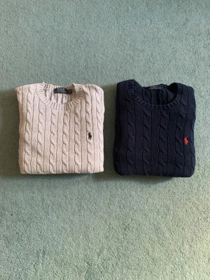 Polo Ralph Lauren kabelstickade tröjor - S -   Säljer två klassiska kabelstickade tröjor från Polo Ralph Lauren i storlek S. En i grå med mörkblå logga och en i marinblå med röd logga. Tillverkade i mjuk 100 % bomull och passar perfekt året runt.  * Storlek: S (regular fit) * Skick: Mycket fint skick, sparsamt använda * Material: 100 % bomull * Färger: Beige & marinblå  350/st eller 600 kr för båda.  Skickas snabbt. Hör gärna av dig om du vill ha fler bilder eller om du har frågor