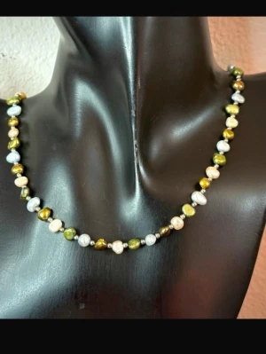 Vintage Halsband med Äkta Barocka Sötvattenspärlor – Flerfärgat 80/90-tal Vintage Retro Boho Luxe - Vintagehalsband med äkta barocka sötvattenspärlor i grönt, vitt, champagne och guldbrunt. Pärlornas oregelbundna former och mjuka lyster ger ett unikt boho-uttryck. Stilen känns 80-/90-tal, men exakt årtal är okänt.  Längd: ca 42 cm Material: sötvattenspärlor och silverfärgad metall Skick: fint vintageskick med lätt slitage på låset. Pärlorna är hela.  Jag prutar inte, men ger gärna paketpris.