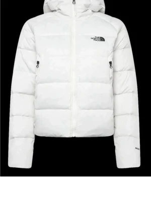 Vit dunjacka från The North Face - Snygg vit dunjacka från The North Face med huva och dragkedja framtill. Jackan har en puffig design, två sidofickor med dragkedja och logga på bröstet. Perfekt för kalla vinterdagar och riktigt varm tack vare dunfyllningen.