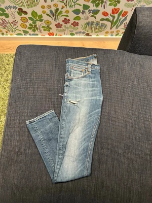 Nudie jeans - Säljer ett par ljusblå nudie jeans, model thin finn. Modellen säljs inte längre. De är ganska tunna vilket är väldigt skönt när det är varmt ute. Passformen är slim fit. De några hål som man kan laga om man vill men nästan snyggare att inte laga. Nypris=1600. Stl w30 l32