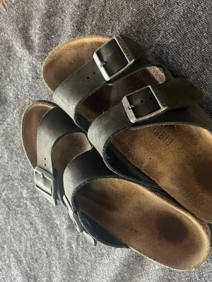 Svarta birkenstock Arizona  - Snygga svarta birkenstock Arizona tofflor. Fotbädden är i kork och innersulan i mocka för extra komfort. Klassisk slip-in modell som passar perfekt till sommaren.