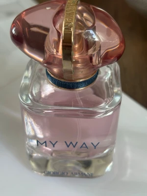 My Way parfym från Giorgio Armani - Säljer en elegant parfymflaska 'My Way' från Giorgio Armani. Flaskan är genomskinlig med ljusrosa parfym och har ett unikt rosa och guldigt lock. Modern och stilren design som passar perfekt på sminkbordet.