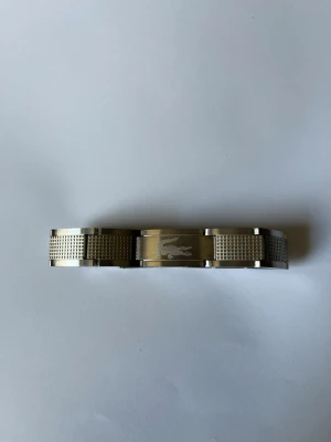 Lacoste armband silver  - Säljer mitt Lacoste armband i rostfritt stål. Det är bara använt ett fåtal gånger därav i mycket bra skick. Det är 20 cm långt men det går att förkorta till 18 cm. Hör av er om ni har några frågor. Mvh Loke