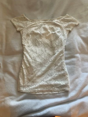 Vit spets topp med kort ärm - Säljer en söt vit topp i spets med korta ärmar och off shoulder. Toppen har ett blommigt spetsmönster och är lätt figurnära. Perfekt att styla med jeans eller kjol för en fräsch look.