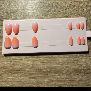 Ombre press-on naglar i rosa och aprikos - Snygga press-on naglar i en mjuk ombre från rosa till aprikos. Naglarna har en oval form och kommer i flera storlekar för perfekt passform. Perfekta för dig som vill ha en fräsch och trendig look utan att gå till salong. Säljes utan tillbehör och låda. Storlekar x2.
