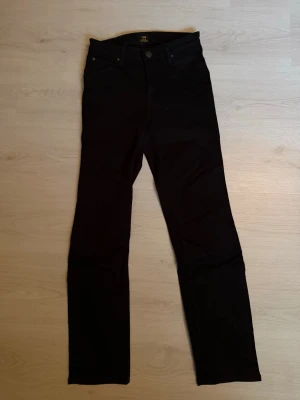 Svarta raka jeans från Lee - Snygga svarta jeans från Lee med rak passform och klassisk femficksdesign. Jeansen har knappgylf med Lee-logga och är tillverkade i ett mjukt denimtyg som sitter skönt. Perfekta för dig som gillar en stilren look.
