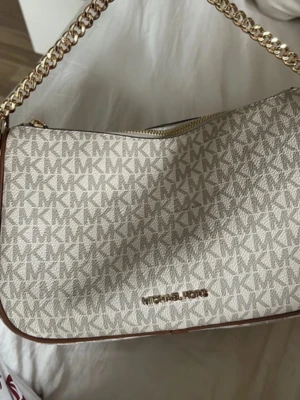 Beige Michael Kors handväska -  Säljer denna fina Michael Kors väska då den tyvärr inte kommer till användning och jag tycker inte riktigt väskan passar just mig. Väskan är i mycket fint skick med minimala tecken på användning. Perfekt storlek för mobil, plånbok och andra vardagssaker. Äkta Michael Kors och redo för en ny ägare. Hör gärna av dig om du har frågor eller vill se fler bilder! ( Kan gå med på att sänka priset vid snabbaffär)