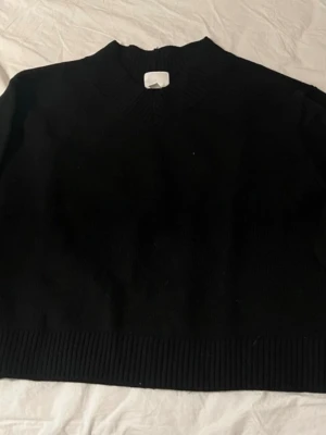 Svart stickad tröja  - Svart stickad tröja. Tröjan har en klassisk rund halsringning och ribbade muddar vid hals och nederkant. 