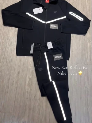 Nike Tech svart set med reflexdetaljer - Nike Tech loungewear set i svart med reflekterande detaljer på både jacka och byxor. Helt ny med prislapp och påse 