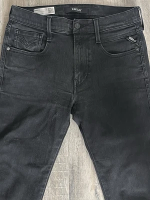 Svarta Replay jeans med smal passform - Snygga svarta jeans från Replay med skön passform och klassisk femficksdesign. Jeansen har diskreta och unika ditaljer och svarta sömmar för en clean look. Tillverkade i stretchigt denimtyg som ger skön komfort och bra rörlighet. Jeansen är knappt andvända och i väldigt bra skicka. Bara att skriva vid funderingar.