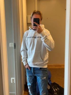 Vit  Sail Racing hoodie - Säljer en vit hoodie från Sail Racing med svart logga och text på bröstet. Hoodien har huva med dragsko och en stor magficka. Tillverkad i mjukt material, perfekt för en avslappnad och sportig stil.