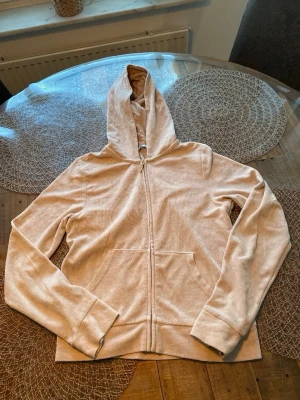 Beige hoodie med dragkedja - En stilren beige hoodie med dragkedja framtill och stora fickor. Hoodien har en klassisk huva och är tillverkad i ett mjukt, bekvämt tyg. Perfekt för en avslappnad look och enkel att matcha med andra plagg.