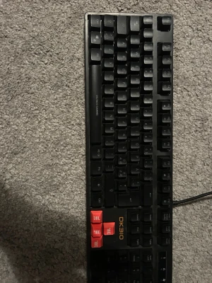 Svart mekaniskt tangentbord DK310 - Säljer ett svart mekaniskt tangentbord DK310 med röda WASD-tangenter. Tangentbordet har en klassisk layout och är anslutet med kabel. Perfekt för gaming eller arbete vid datorn. Robust design i plast och tydliga tangenter.