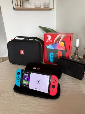 Nintendo Switch OLED 320GB + tillbehör och spel - Säljer en Nintendo Switch OLED 320 GB i mycket fint skick! Knappt använt. Konsolen kommer med två Joy-Cons i färgerna neonblå och neonröd. Medföljer gör även en dockningsstation för att ansluta konsolen till TV:n. Förvaringsväska för konsolen och en större väska för tillbehör ingår. Två Joy-Con grepp för bekvämare spelupplevelse samt två handledsremmar för Joy-Cons ingår också. Två spel, Super Mario Odyssey och FIFA 18, medföljer. Dessutom ingår ett rött fodral för förvaring av spelkassetter. 