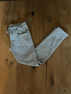 Ljusgråa skinny jeans - Säljer ett par ljusgråa skinny jeans med klassisk femficksdesign och smal passform. Jeansen har bälteshällor och en diskret detalj på bakfickan. Perfekta för en clean och stilren look.