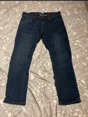 Mörkblå jeans från Pier One - Snygga mörkblå jeans från Pier One med klassisk femficksdesign och raka ben. Jeansen har en stilren look med diskreta sömmar och är tillverkade i ett mjukt denimtyg som ger en bekväm känsla hela dagen.