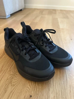 Nike sneakers  - Snygga helsvarta Nike sneakers med lågt skaft. Ovandelen är i mesh och syntetmaterial för bra andningsförmåga och komfort. Klassisk Nike-logga på sidan och tålig yttersula. Perfekta för en sportig och clean look.
