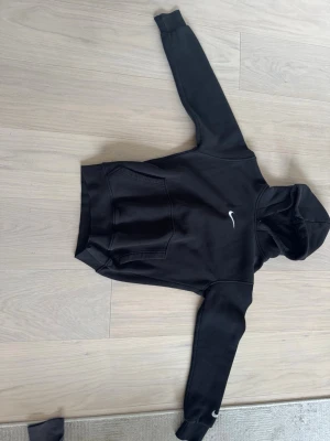 Svart hoodie från Nike med logga - Säljer en svart hoodie från Nike med vit logga på bröstet och ärmen. Hoodien har en klassisk känguruficka framtill och huva. Tillverkad i mjukt material som passar perfekt till en avslappnad stil.