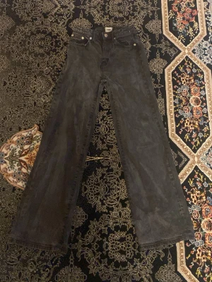 Svarta utsvängda jeans - Säljer ett par svarta jeans med utsvängda ben och klassisk femficksmodell. Jeansen har hög midja och raka, vida ben för en avslappnad och trendig look. Perfekta till sneakers eller boots.