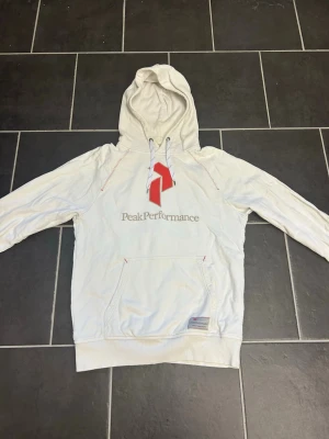 Hoodie - Vit hoodie ifrån Peak Performance med storleken M. Skriv vid intresse eller frågor!
