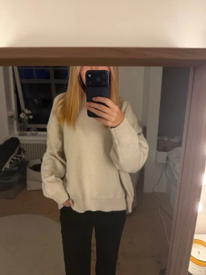 Beige oversized stickad tröja - Mysig beige stickad tröja med avslappnad, oversized passform och rund hals. Tröjan har långa ärmar och ribbade muddar vid ärmslut och nederkant. Perfekt för lager på lager under kyliga dagar.