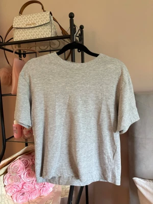 Grå basic t-shirt från Gina Tricot - En enkel och stilren grå t-shirt från Gina Tricot, basically basics-kollektionen. T-shirten har rund halsringning, korta ärmar och är gjord i mjukt bomullsmaterial. Perfekt till alla outfits och lätt att matcha.