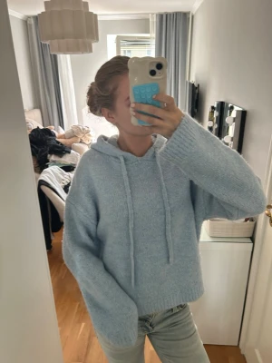 Ljusblå fluffig hoodie - Mysig ljusblå hoodie med huva och dragsko. Tröjan är stickad i ett fluffigt material och har en avslappnad passform med långa ärmar. Perfekt för dig som gillar en chill och comfy stil.