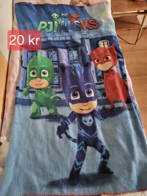 PJ Masks filt med motiv - Mysig filt med färgglatt PJ Masks-motiv som visar karaktärerna Gecko, Catboy och Owlette. Filtens färger är blå, grön, röd och lila och materialet är mjuk fleece. Perfekt för att mysa i soffan eller som överkast till barnrummet.