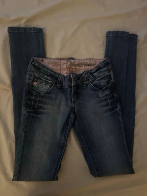 Mörkblå skinny jeans med slitningar - Säljer ett par mörkblå skinny jeans med snygga slitningar och tvättade detaljer. Jeansen har fem fickor, låg midja och smala ben. Materialet är klassisk denim med stretch för skön passform. Perfekta till en avslappnad stil.