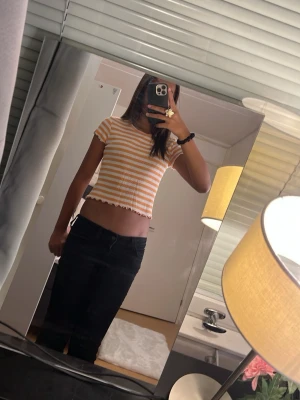 Randig ribbad t-shirt från Lindex - Säljer en ribbad t-shirt från Lindex med orange och vita horisontella ränder. T-shirten har korta ärmar och vågig kant nertill och vid ärmslut. Perfekt för dig som gillar färg och mönster!