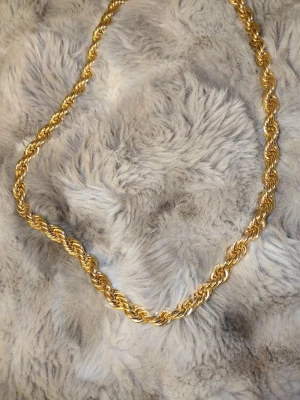 Guldfärgat tvinnat halsband 8MM 60CM - Snyggt halsband i guldfärgad metall med tvinnad kedja som ger en chunky och trendig look. Perfekt för att lyfta vilken outfit som helst med lite extra bling. Halsbandet har en enkel ringlås och känns rejält utan att vara för tungt.