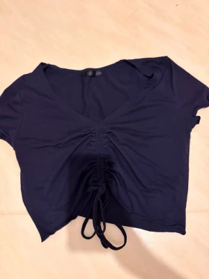 Mörkblå crop top från SHEIN - Säljer en mörkblå crop top från SHEIN med djup V-ringning. Toppen har snygg rynkning och knytband framtill. Perfekt nu till sommaren. 