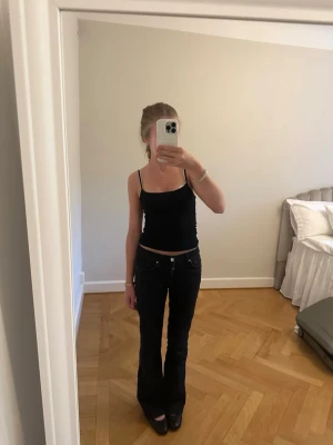 Svarta bootcut jeans med hög midja - Säljer ett par svarta bootcut jeans med hög midja och klassisk femficksdesign. Jeansen har en smickrande passform och lätt utsvängda ben, perfekta till både sneakers och boots. Materialet är stadigt denim i svart tvätt. Snygga och trendiga jeans för alla tillfällen. (Low flare waist s length 31)