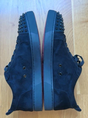 Svarta Christian loubs Med Spikar - Svarta sneakers i mocka med coola svarta nitar på tån och klassisk röd sula. Har inte boxen men fraktas med en box. Fraktas samma dag.       ( Använt ) Kan passa 43